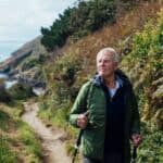 A senior man using hiking poles, on a hike on a coastal path along the coastline of Cornwall.