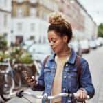 Shot of an young mixed-race woman using her cellphone while out cycling through the city