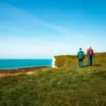 Rear view image depicting two men hiking together with the stunning backdrop of Seven Sisters cliffs in the south of England.